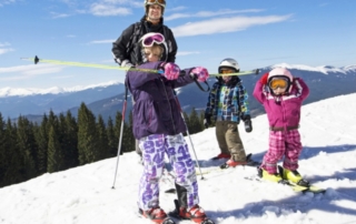 Big Sky Skiing: A dad and his kids enjoy the top of a skiing hill at Big Sky Resort.