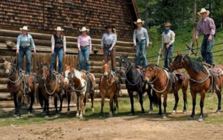 Ranch Vacations in Montana: A group of seven ranch hands stand upon their saddles outside of the stable at 320 Guest Ranch in Gallatin Gateway, MT.